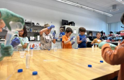 Students standing at a table pipetting liquid into a small container.