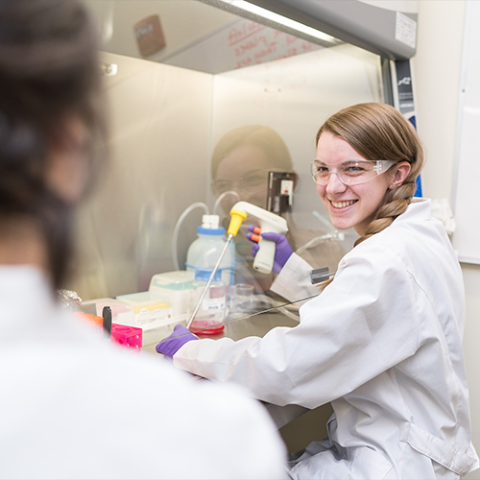 Smiling student wearing a lab coat working at a lab station