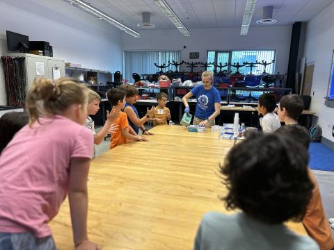 Students standing around a table watching a science demonstration.