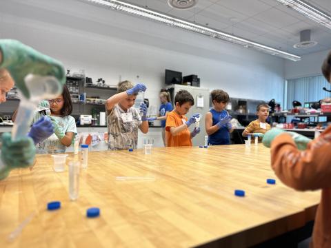 Students standing at a table pipetting liquid into a small container.